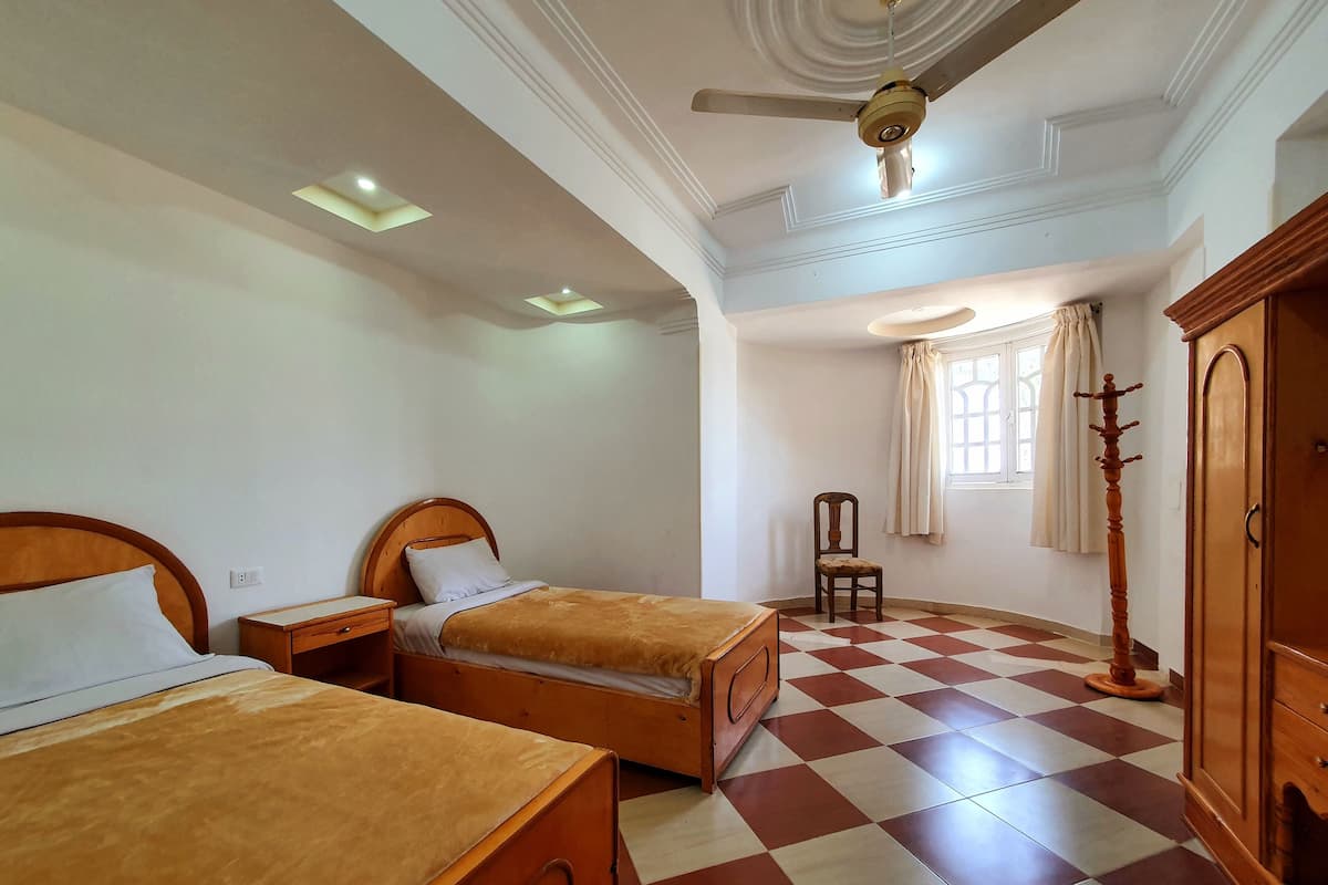 A hotel room with two wooden beds, a wooden wardrobe, a chair, and a ceiling fan.