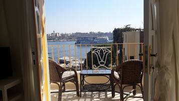 A balcony with wicker chairs and a table, overlooking a waterfront with boats and buildings.