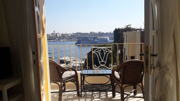 Un balcón con sillas de mimbre y una mesa, con vista a un muelle con barcos y edificios.