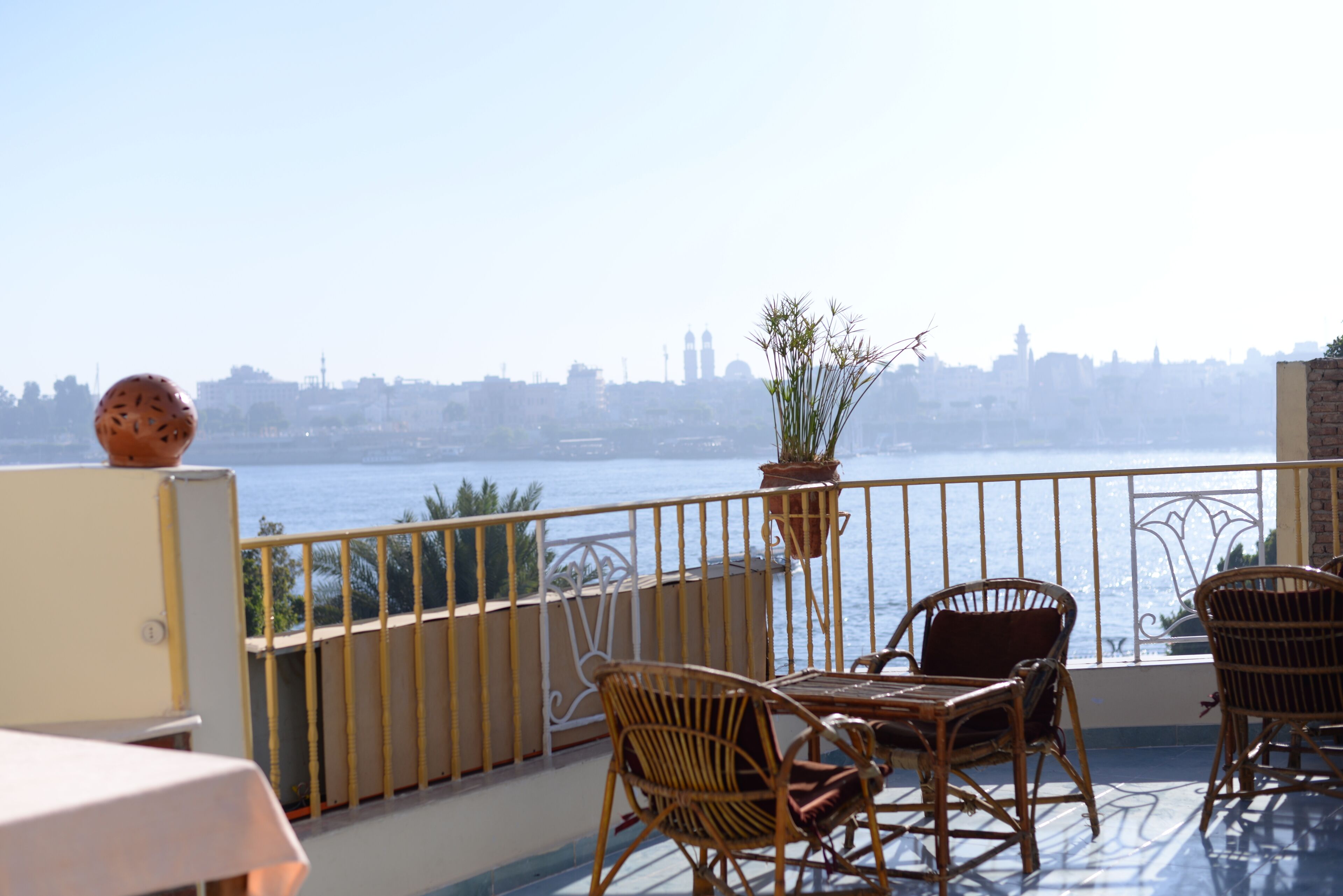 A balcony with wicker furniture, a potted plant, and a view of a city skyline across a body of water.
