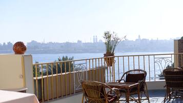 A balcony with wicker furniture, a potted plant, and a view of a city skyline across a body of water.