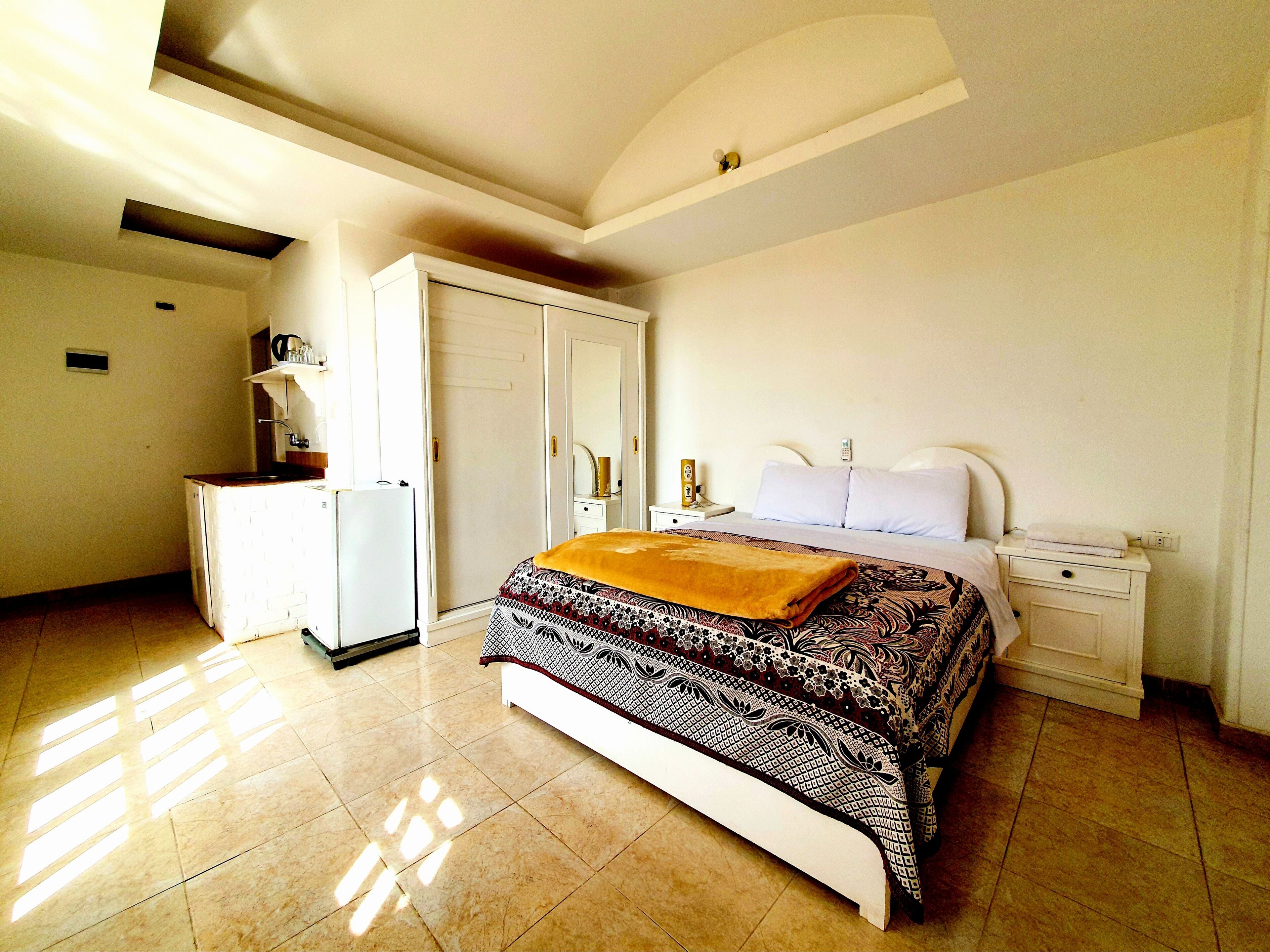 A bedroom with a bed, bedside tables, a wardrobe, and a small kitchenette area.