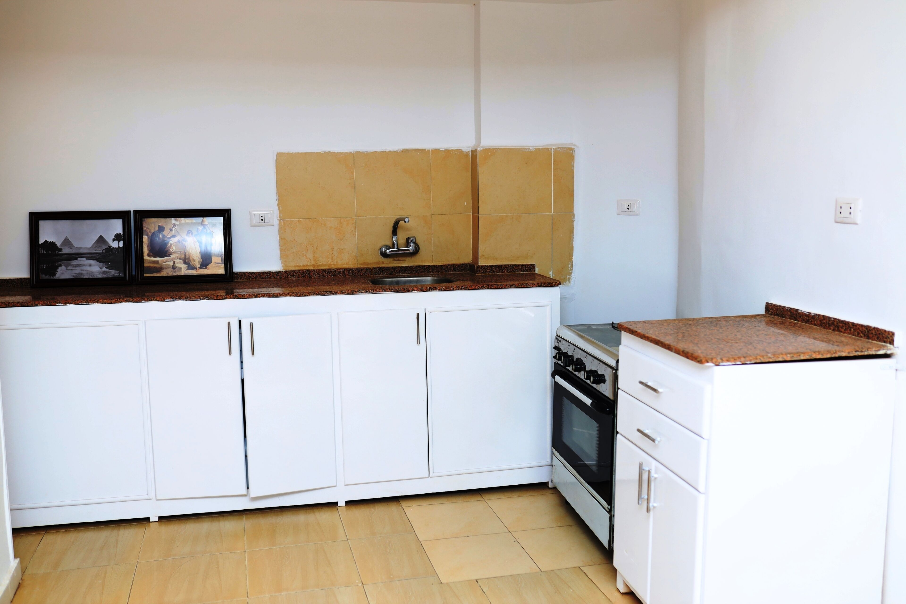 Una cocina compacta con armarios blancos, encimera de granito, horno empotrado y un lavabo.