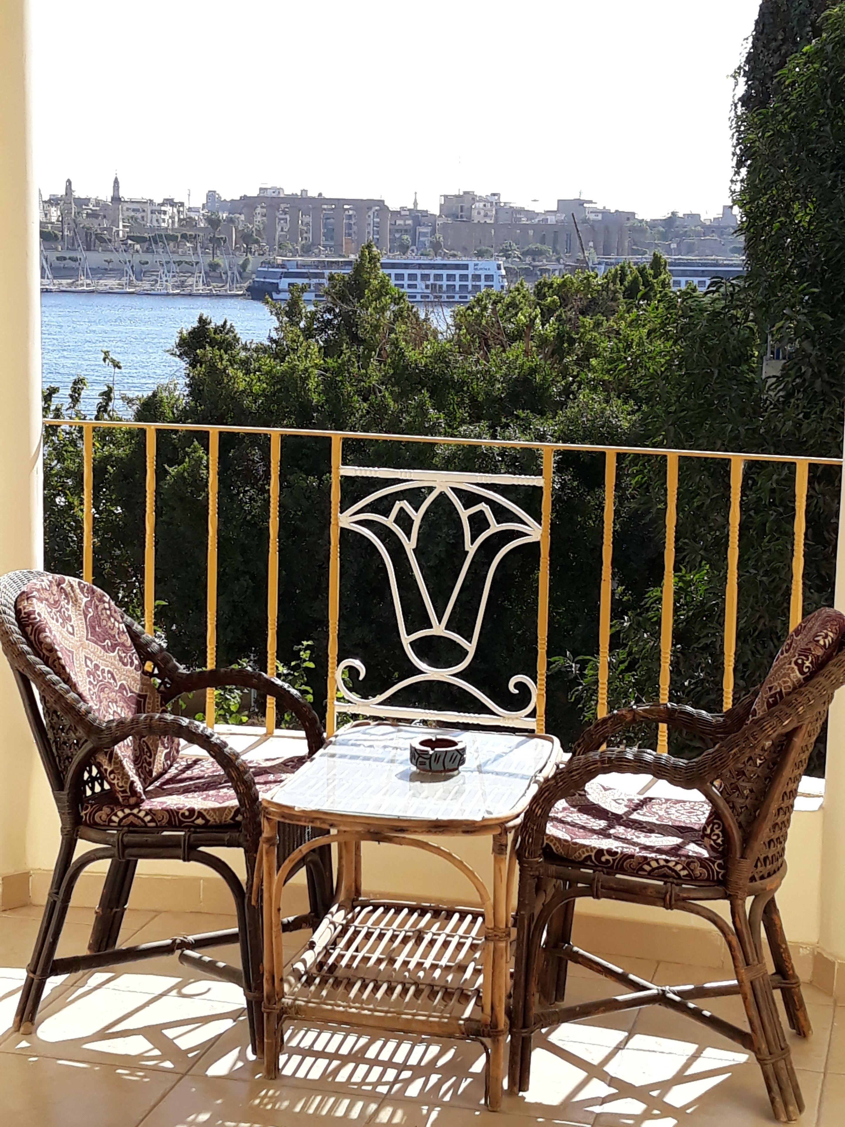 Ein Balkon mit Korbstühlen und einem kleinen Tisch, der auf einen Stadtblick und ein Gewässer hinausblickt.
