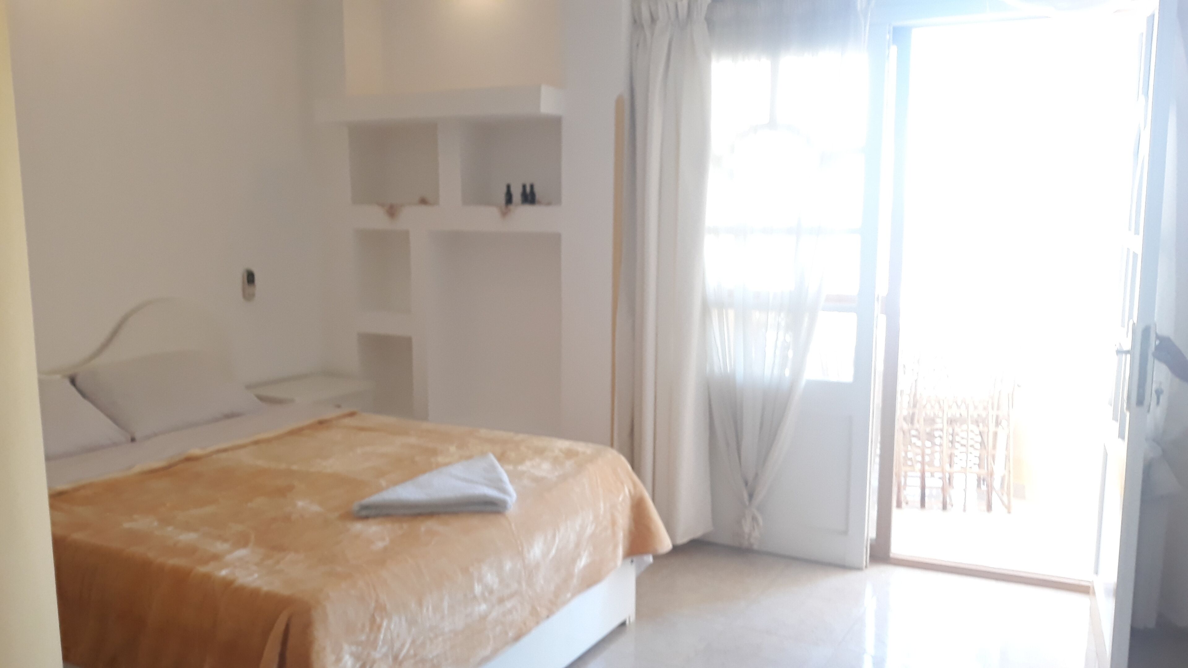A bedroom with a bed, a nightstand, a built-in shelf, and a sliding glass door to the outside.