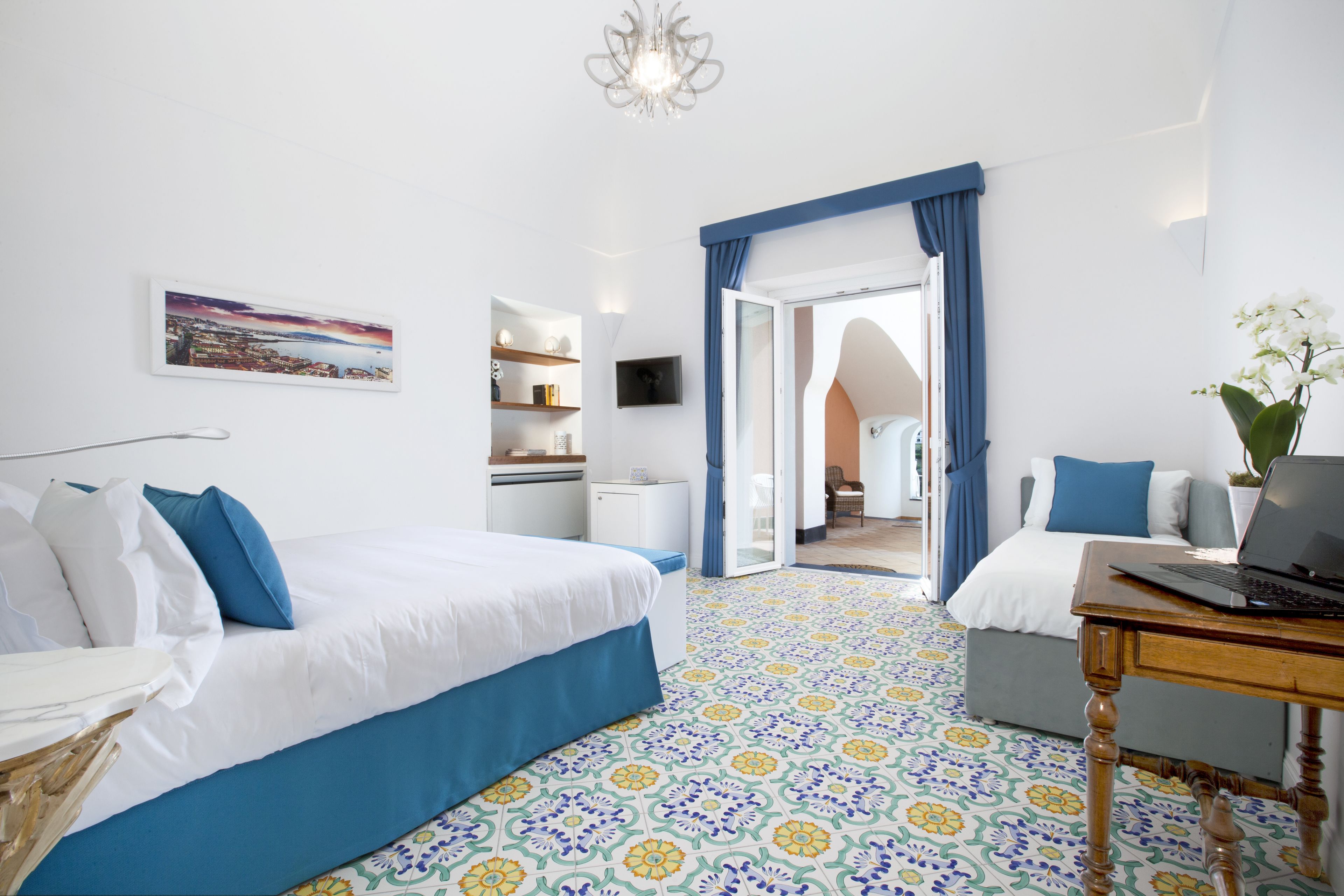 Quarto de hotel com cama, escrivaninha com laptop, cadeira, mesa pequena, TV e vista da cidade pela janela.