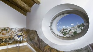 A room with a round window offering a view of a hillside town. - Il Moro di Positano (Positano)
