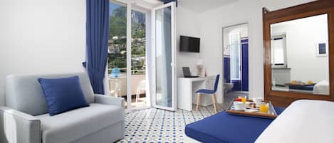 Habitación de hotel con sofá, cama, escritorio con una computadora portátil, bandeja con alimentos para el desayuno y vista al exterior.