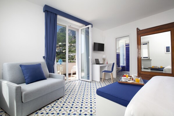 Une chambre d’hôtel avec un canapé, un lit, un bureau avec un ordinateur portable, un plateau avec des articles pour le petit-déjeuner et une vue sur l’extérieur.