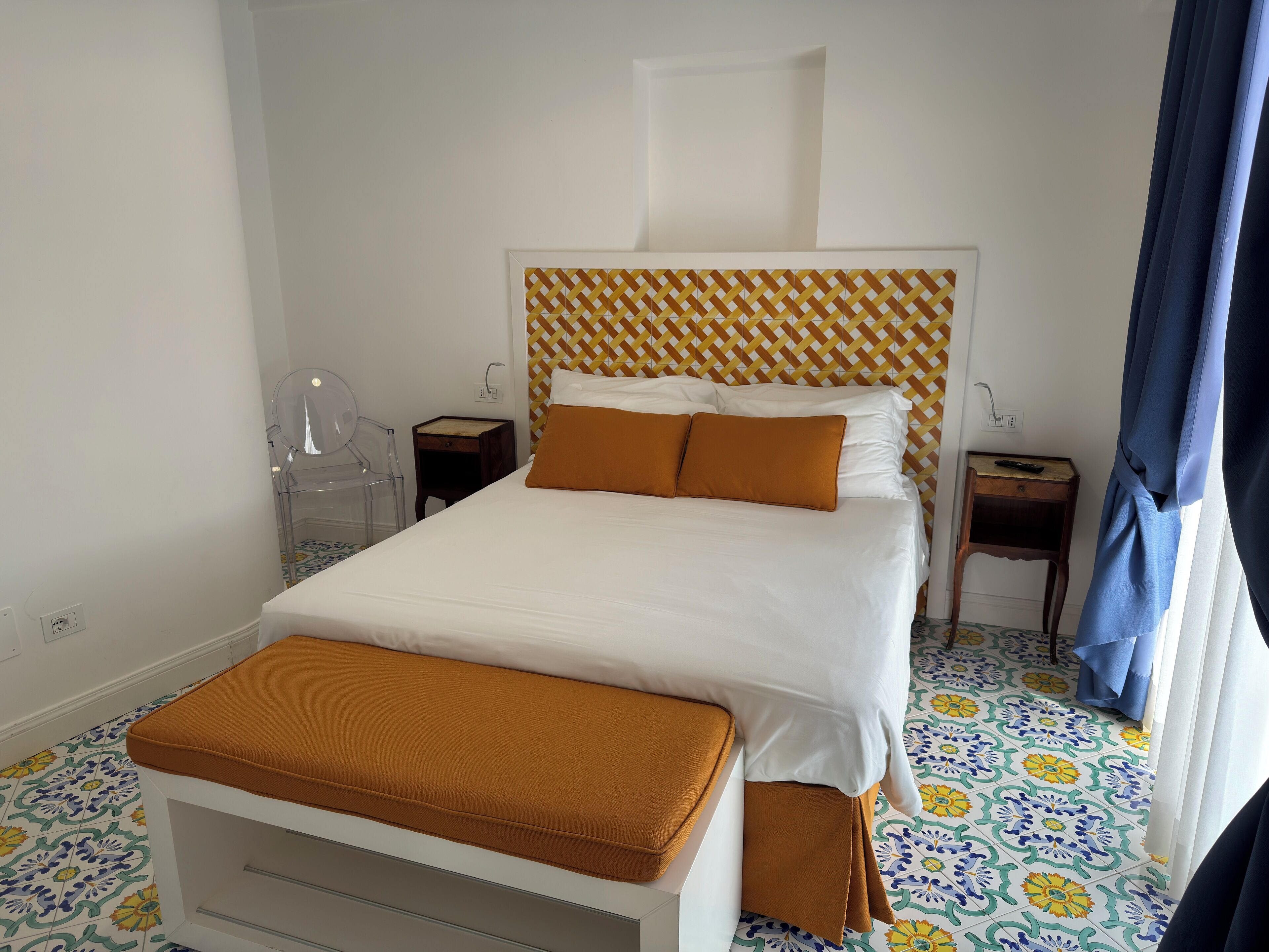 Una camera d'albergo ordinata con un letto, un comodino, una sedia e un tavolino con un telecomando.