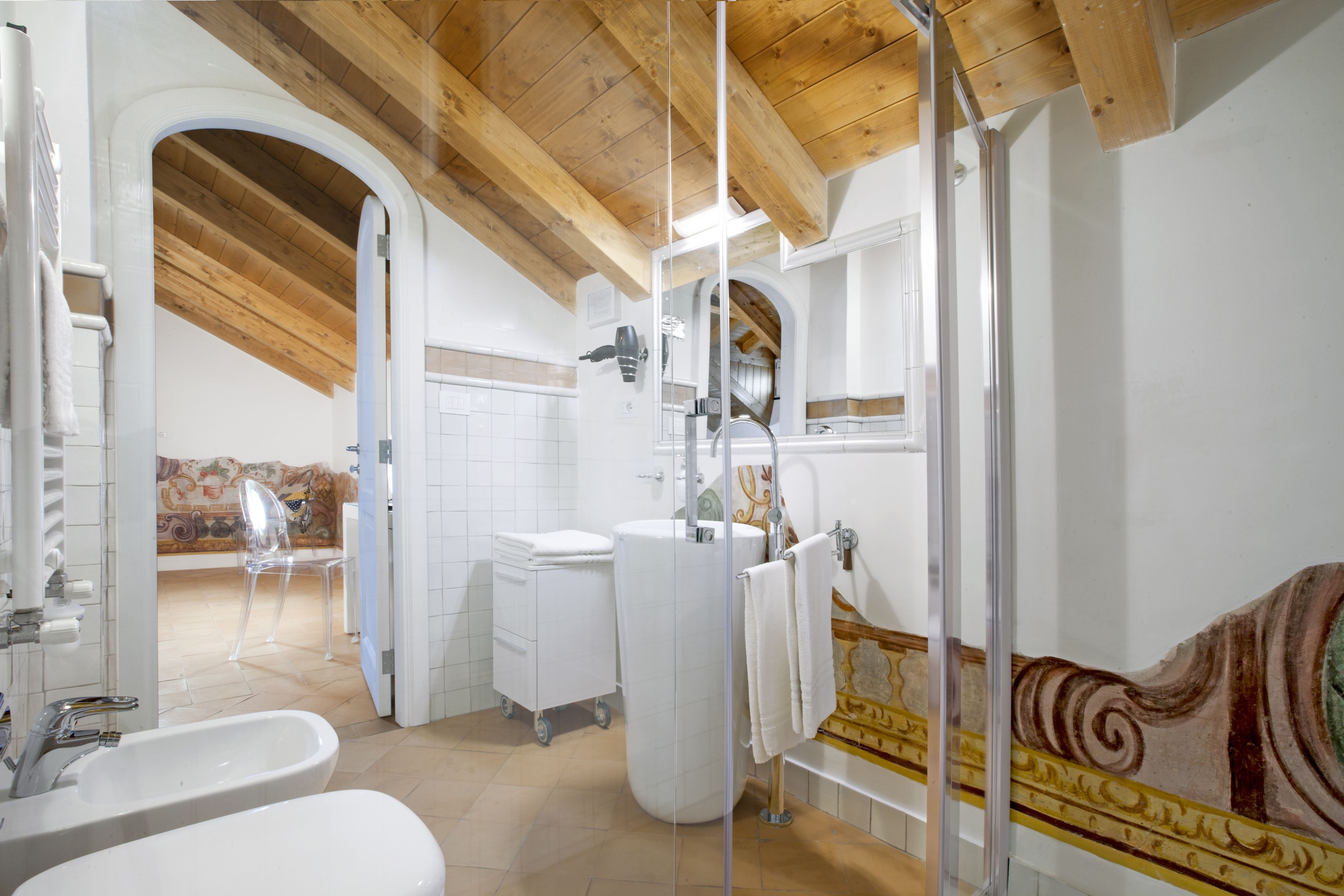 Un baño con techo de madera, azulejos blancos, un lavamanos, un inodoro y una zona de ducha.