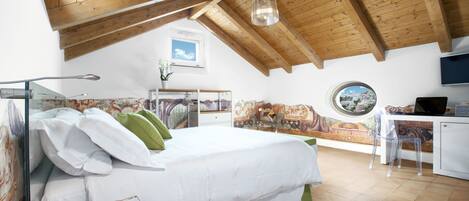 A bedroom with a wooden ceiling, a bed with white bedding, a desk with a chair, and a view through a window.