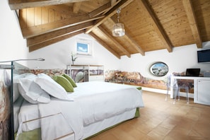 Une chambre avec un plafond en bois, un lit avec une literie blanche, un bureau avec une chaise et une vue par la fenêtre.