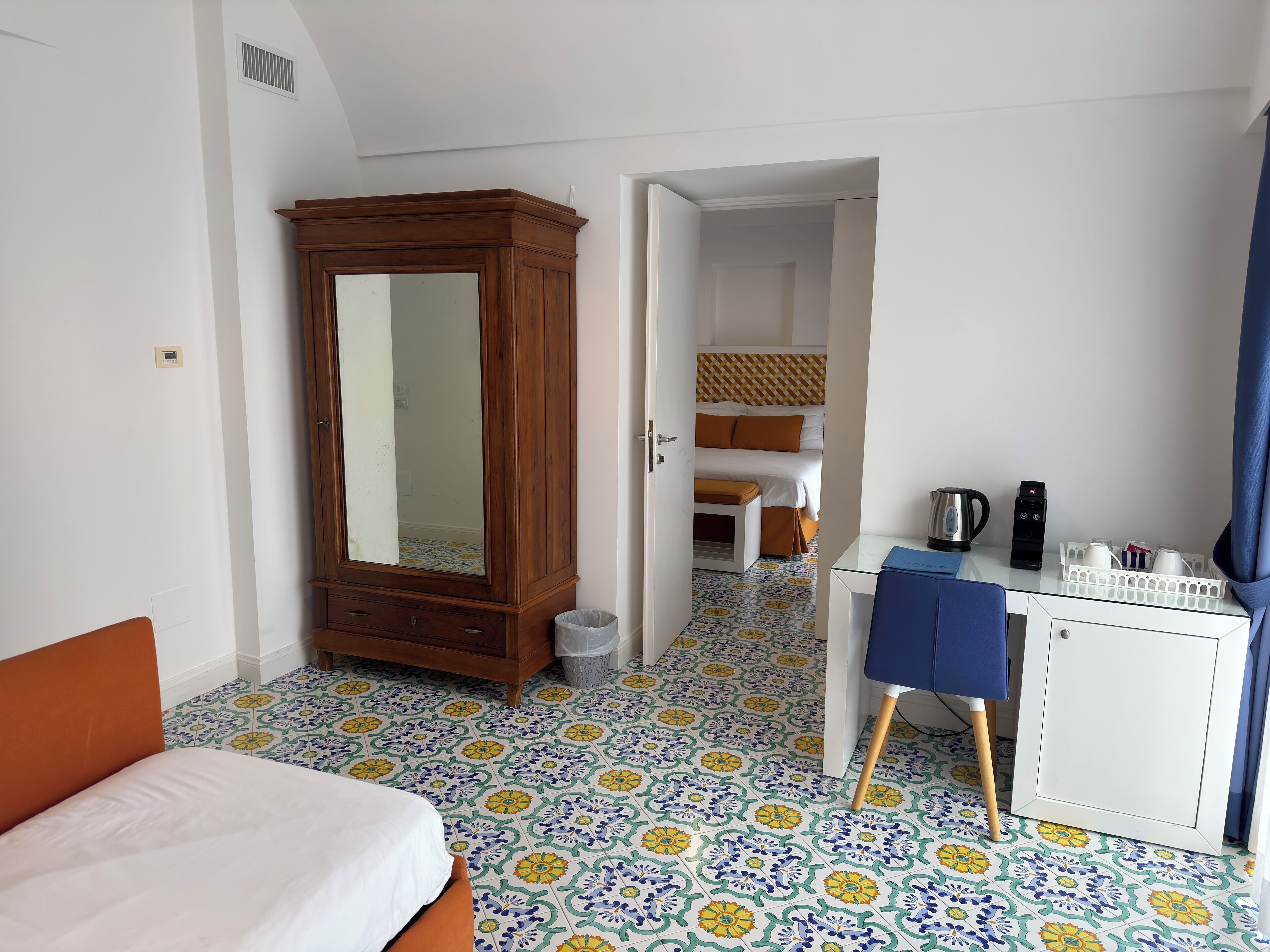 Une chambre d’hôtel comprenant un lit, une armoire, un bureau avec une machine à café et une salle de bain visible à travers une porte ouverte.