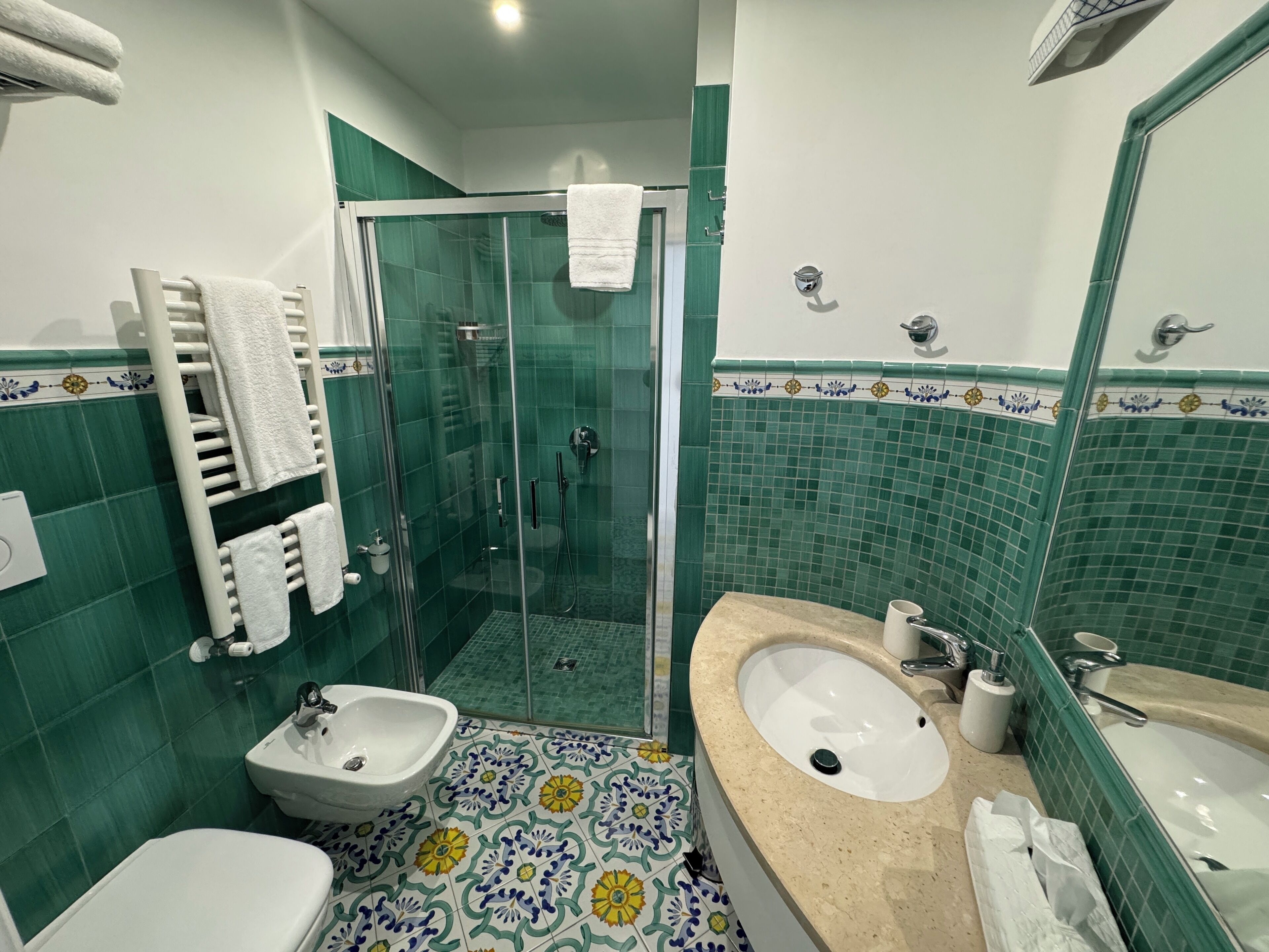 A bathroom with a glass-enclosed shower, a sink, a bidet, and a toilet.