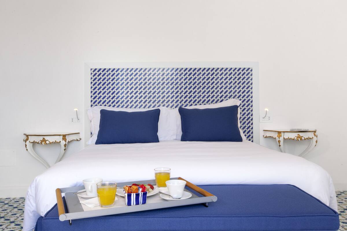 A neatly made bed with a tray of breakfast items, including orange juice and a cup of coffee, on a white and blue patterned headboard.