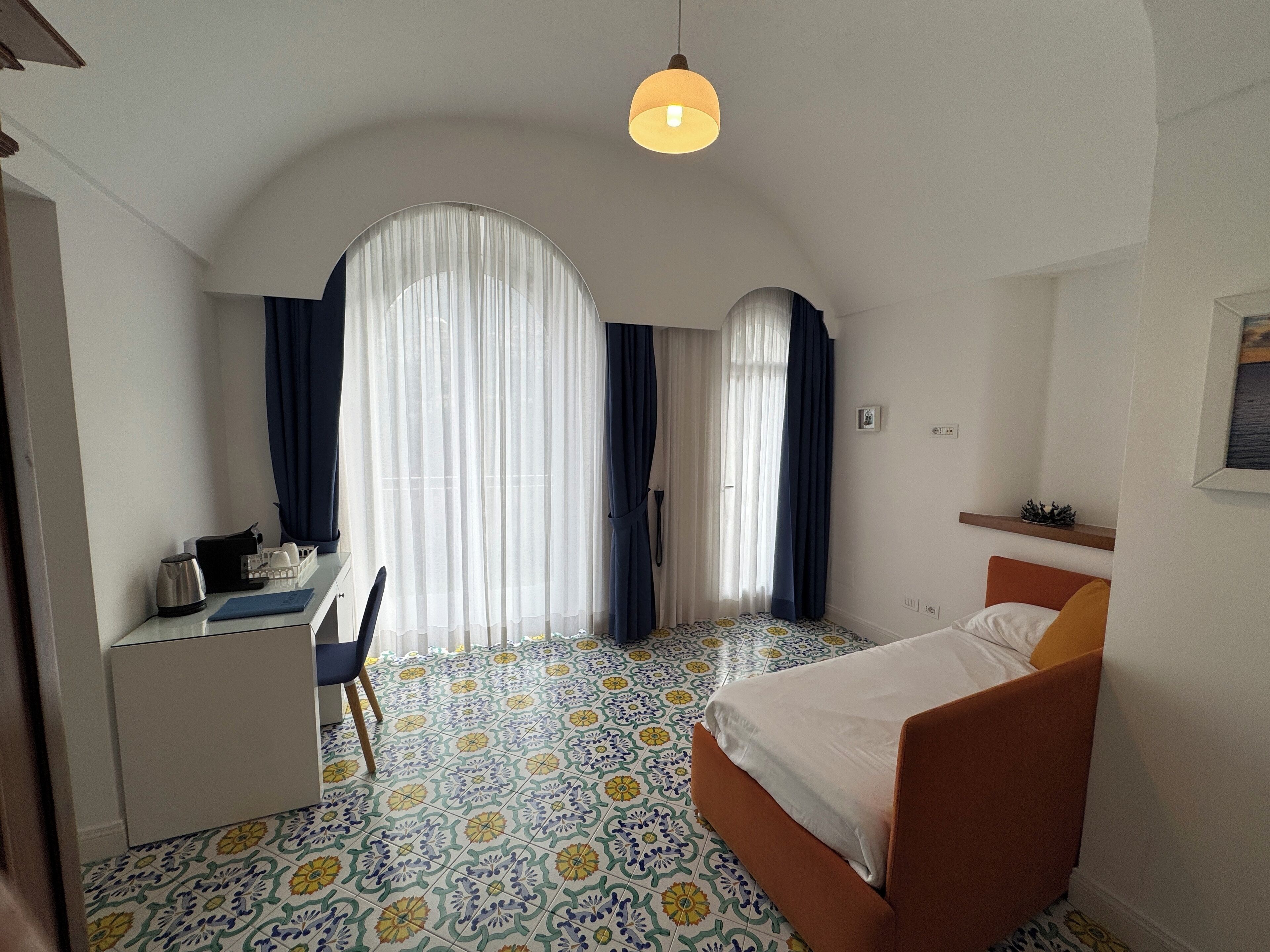 A hotel room with a bed, a desk, and a chair. There are two windows with curtains.