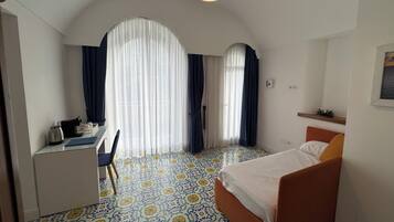 A hotel room with a bed, a desk, and a chair. There are two windows with curtains.