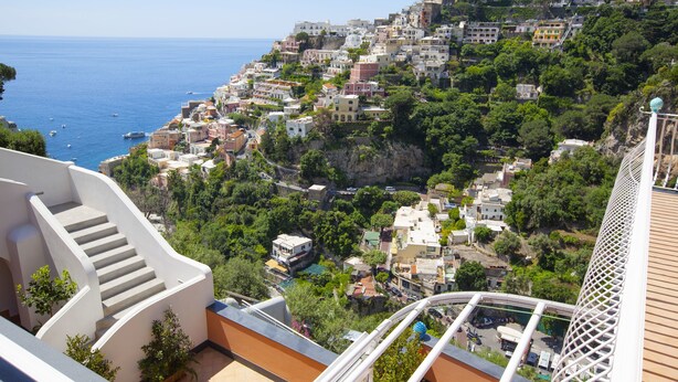 A coastal town with buildings on a hillside, a clear view of the sea, and a staircase leading to a balcony. - Il Moro di Positano (Positano)
