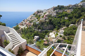 Une ville côtière avec des bâtiments construits sur une colline, une vue dégagée sur la mer et un escalier menant à un balcon.