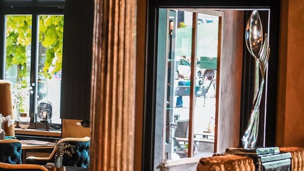 Ein Restaurantinneres mit einem runden Tisch, gepolsterten Sitzgelegenheiten, einer hohen Säule und Blick auf die Straße.