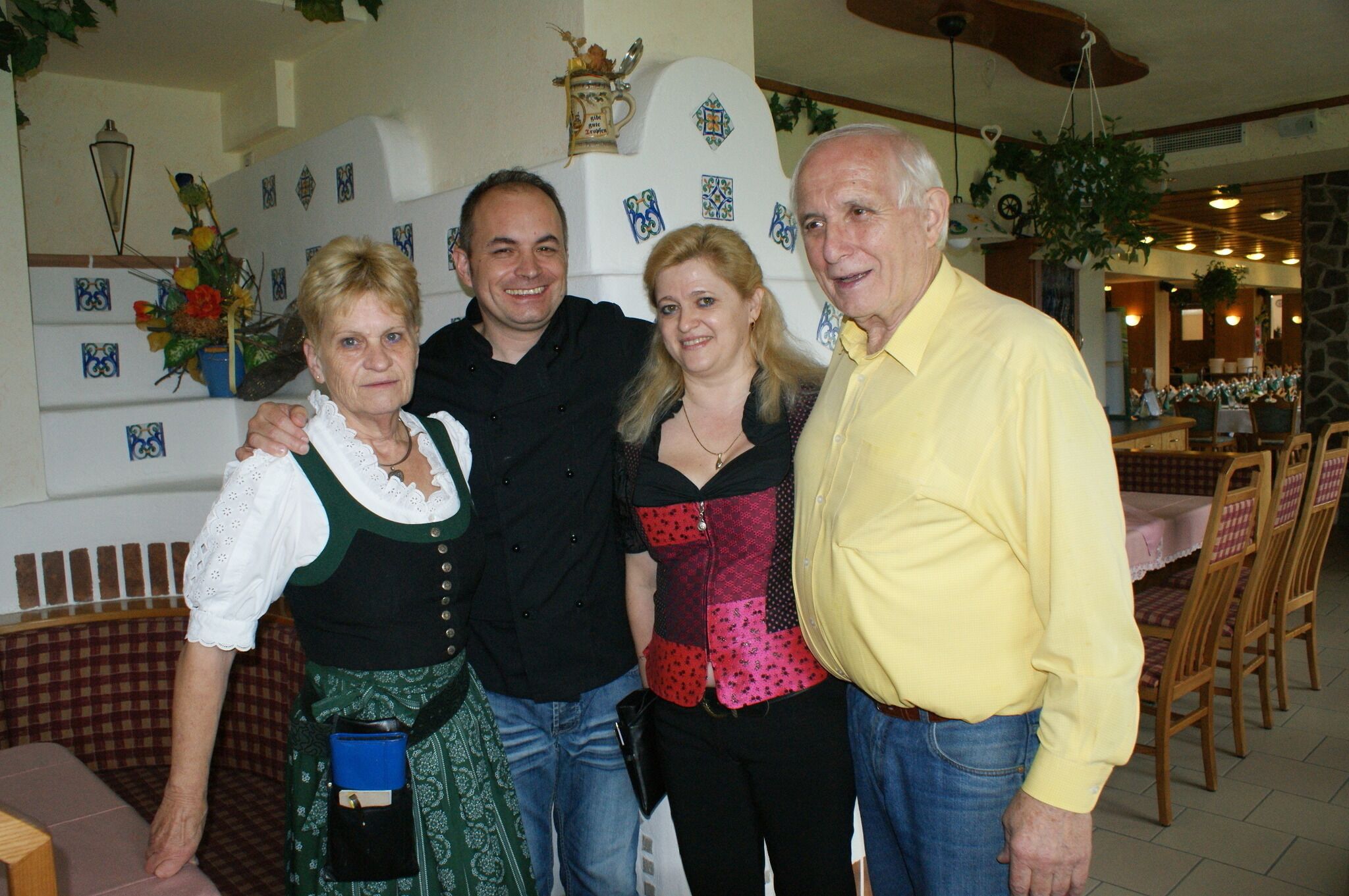 A group of people in a dining area with a checkered bench, a stone wall, and a hanging plant.