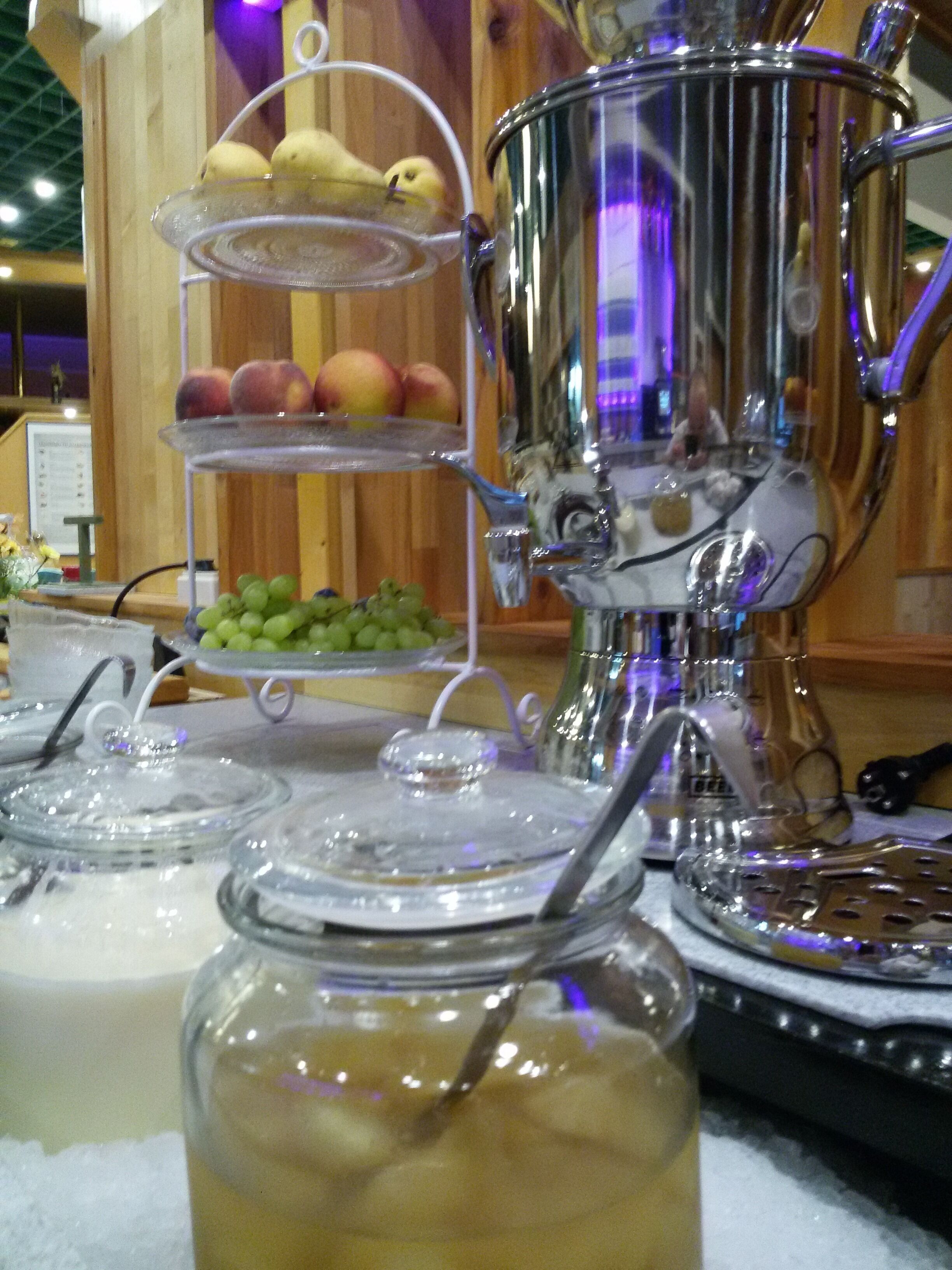 A buffet setup with a fruit display, a beverage dispenser, and glass containers with utensils.