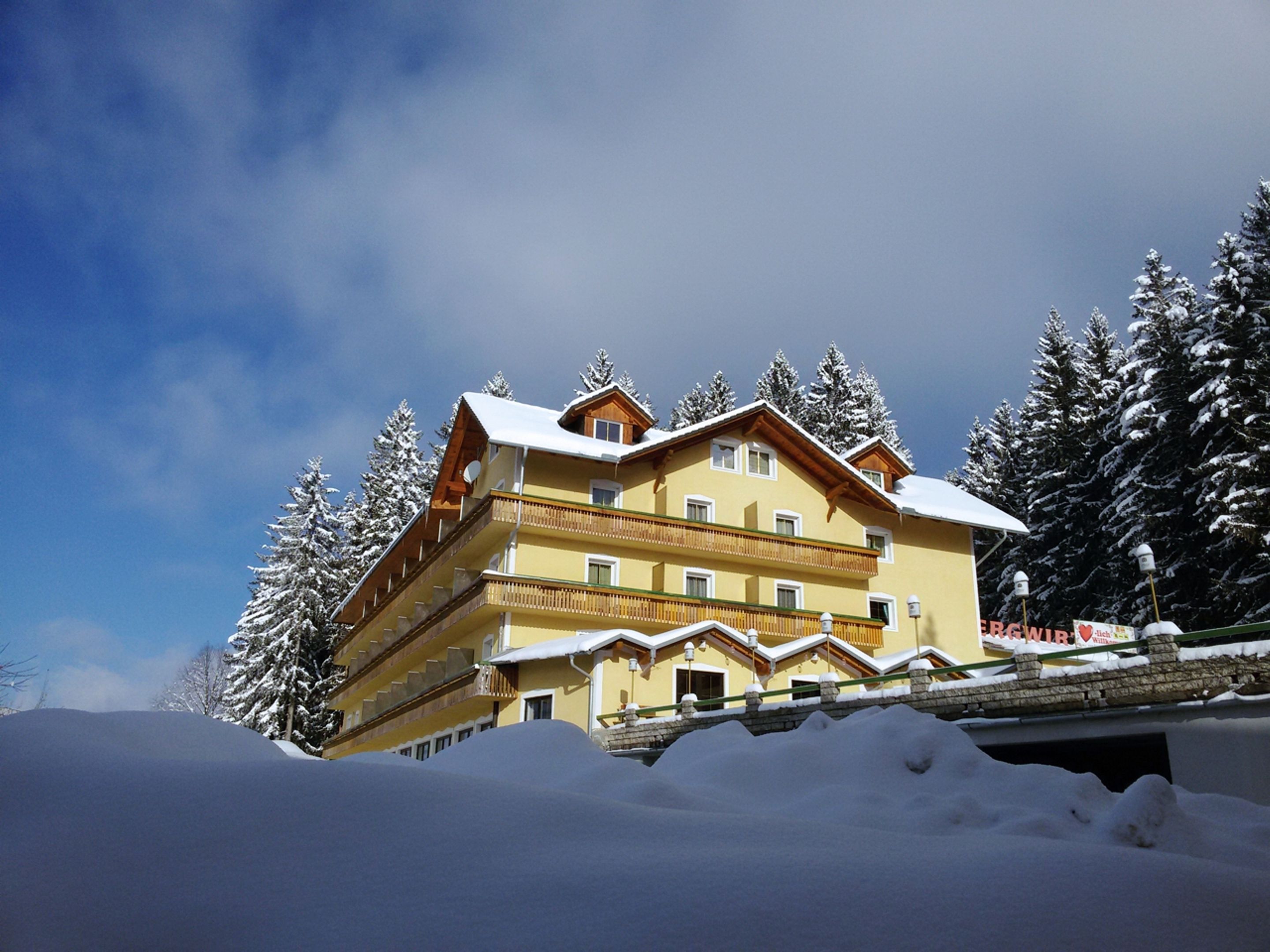 A multi-story hotel with balconies, surrounded by snow-covered trees and a clear sky.