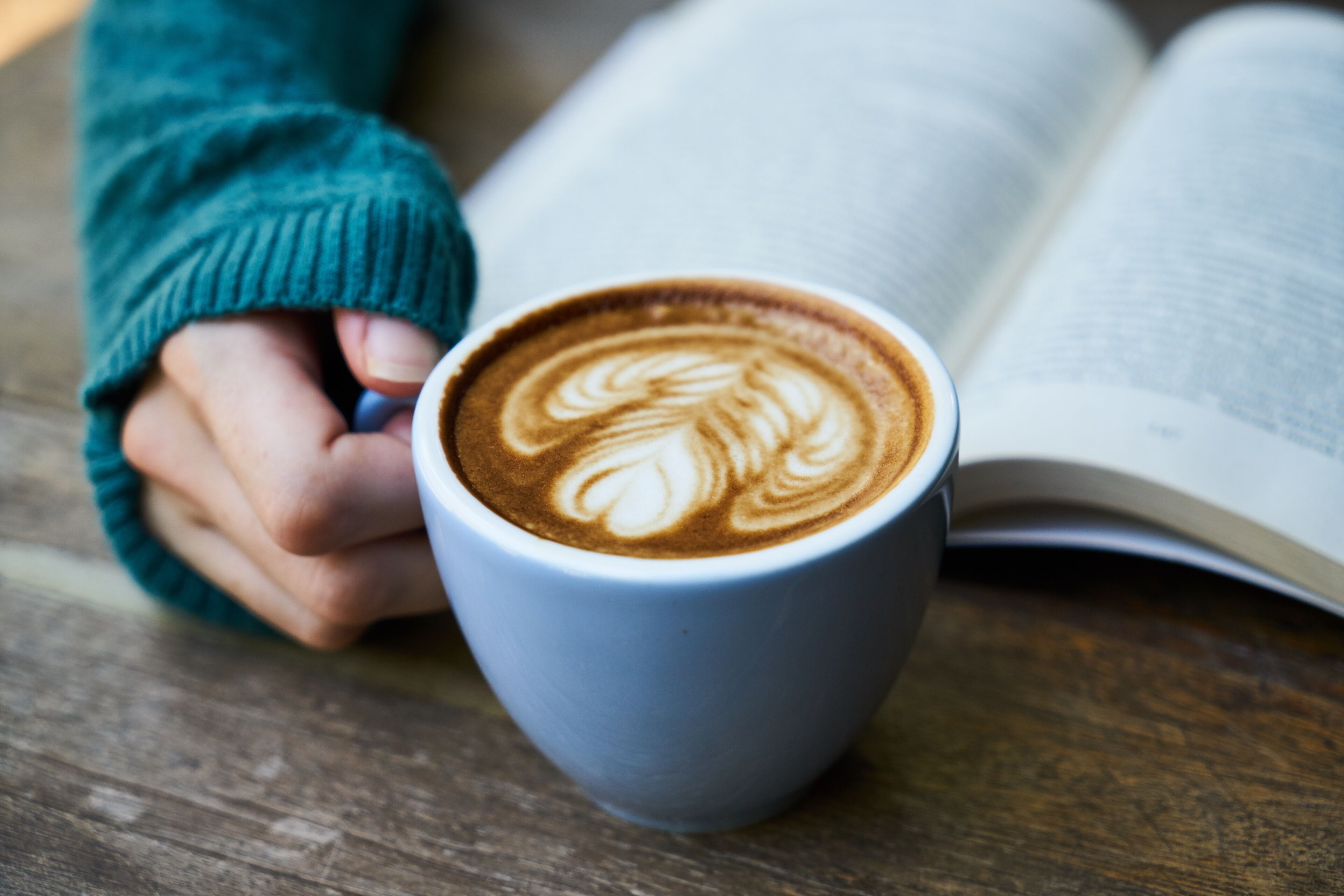 A cup of coffee with latte art on a wooden table next to an open book.