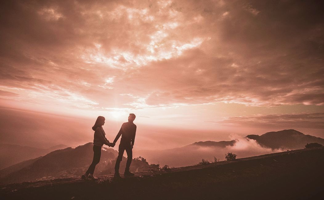 Una pareja tomados de la mano en la cima de una colina, con el atardecer de fondo.