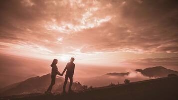 Una pareja tomados de la mano en la cima de una colina, con el atardecer de fondo.