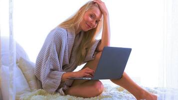 A person sitting on a bed with a laptop, surrounded by pillows and a white blanket.