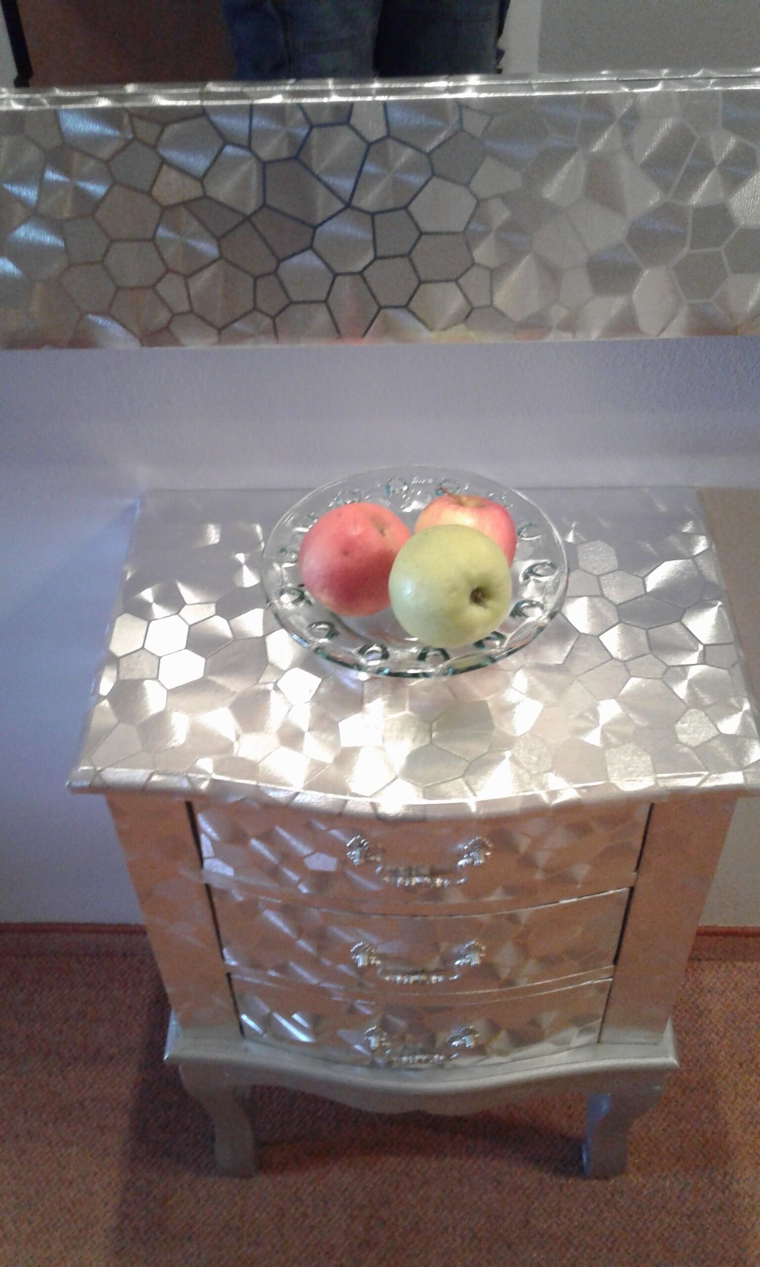 A metallic, hexagonal-patterned cabinet with a glass top holding two apples.
