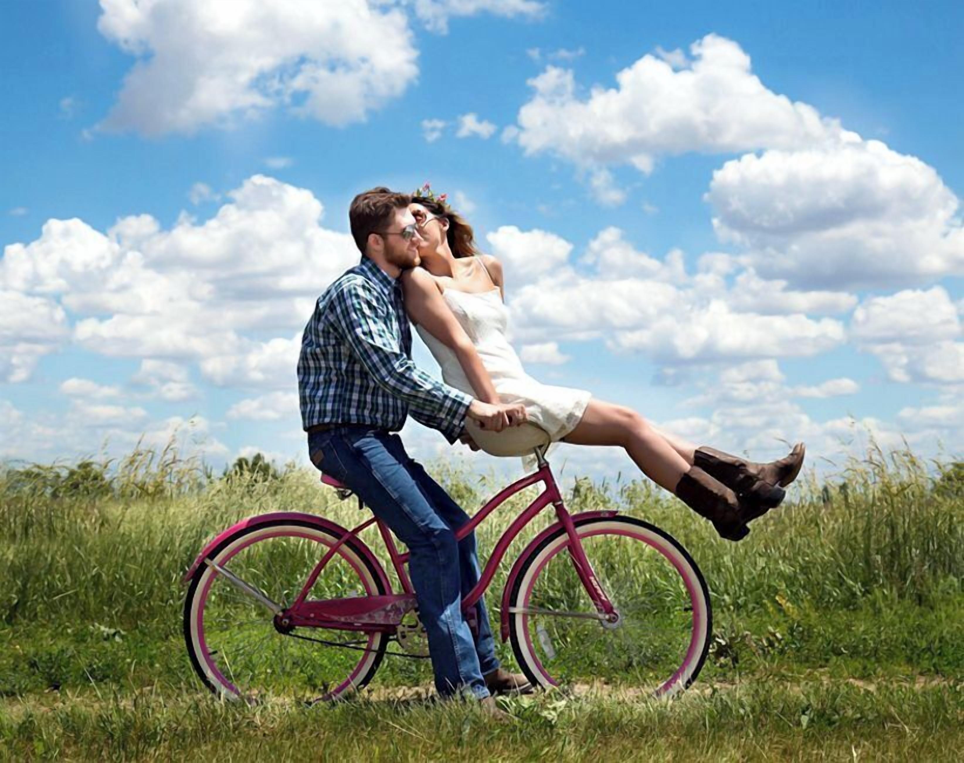 Una pareja en bicicleta en un campo cubierto de hierba, bajo un cielo despejado.