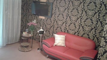 A living room with a red sofa, a small round table with a vase of flowers, and a television mounted on the wall.