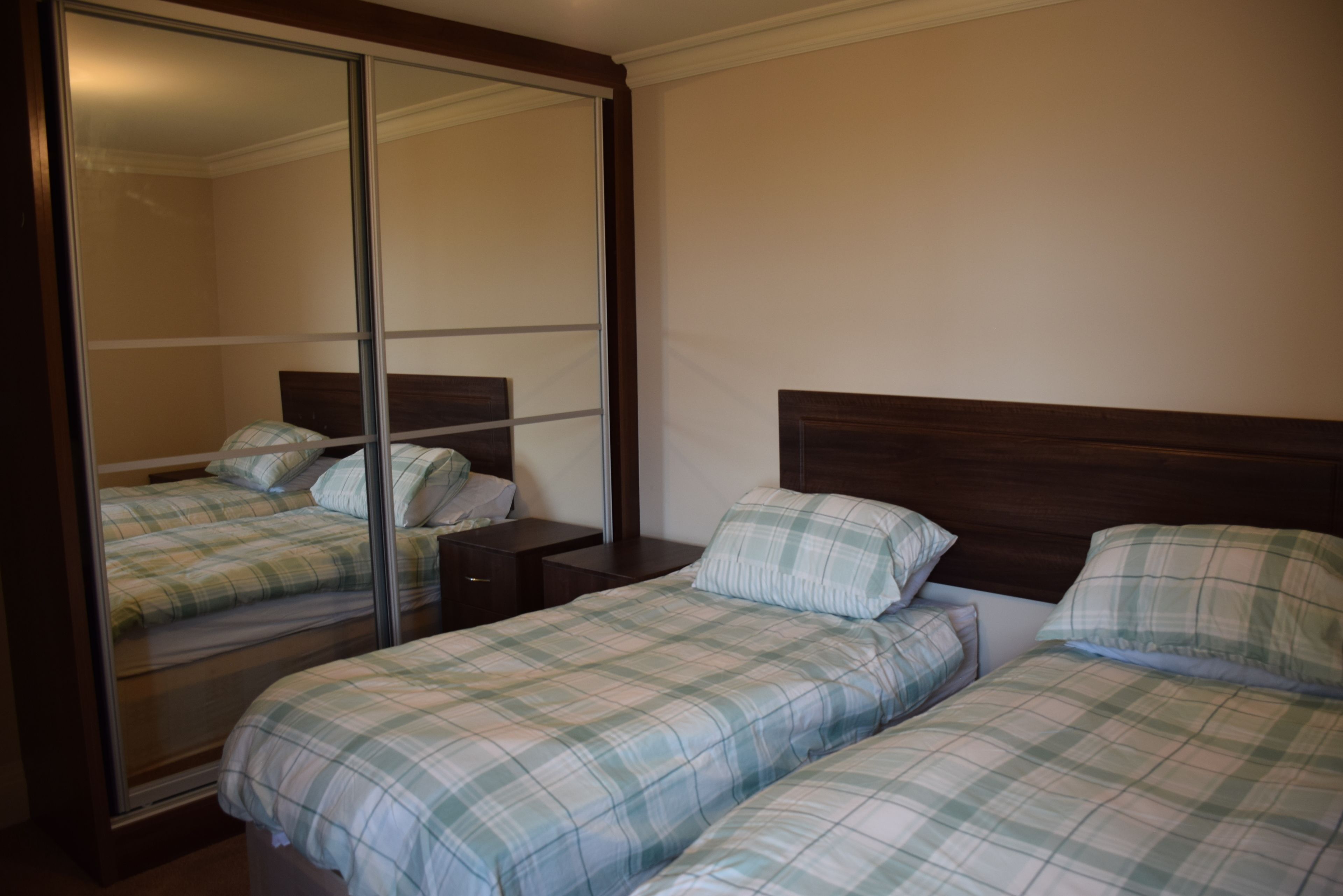 A bedroom with two beds, a large mirror, and a wooden headboard.