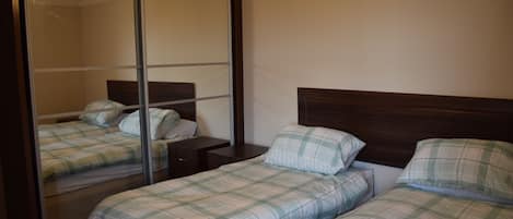 A bedroom with two beds, a large mirror, and a wooden headboard.