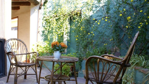 A patio with wicker chairs and a table, surrounded by greenery and a wall with climbing plants.