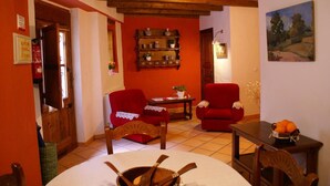 A cozy living room with red chairs, a wooden table, and a shelf with decorative items.