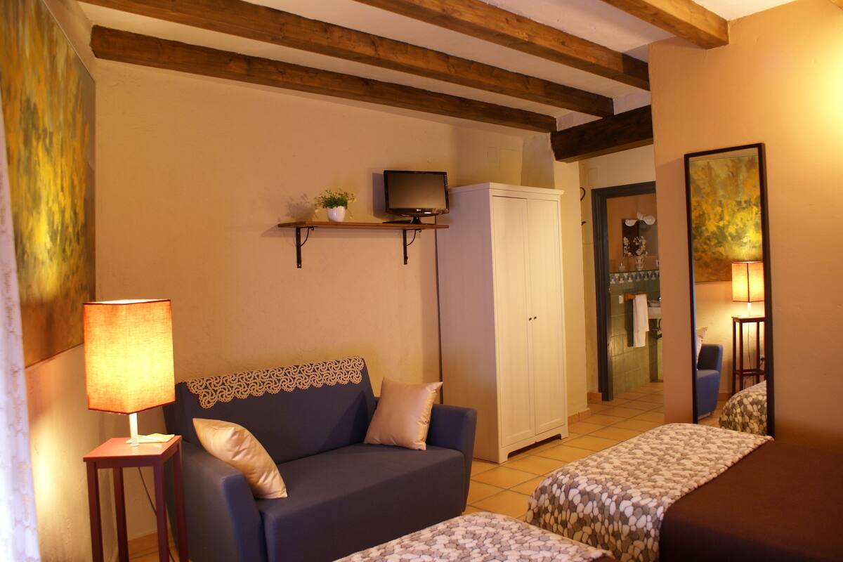 A cozy room with a sofa, a bed, a TV on a shelf, and a cabinet.