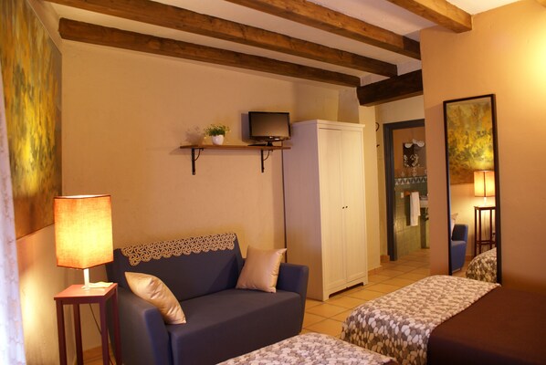 A cozy room with a sofa, a bed, a TV on a shelf, and a cabinet.