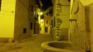 A narrow street with buildings on either side, a street lamp, and a large stone well in the foreground.