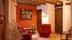 A cozy living room with a red armchair, a wooden shelf with decorative plates, and a tiled floor.
