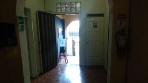 A hallway with a tiled floor, a door with a sign indicating a men's restroom, and a fire extinguisher mounted on the wall. - Krishna Hostal - Hostel (Quito)