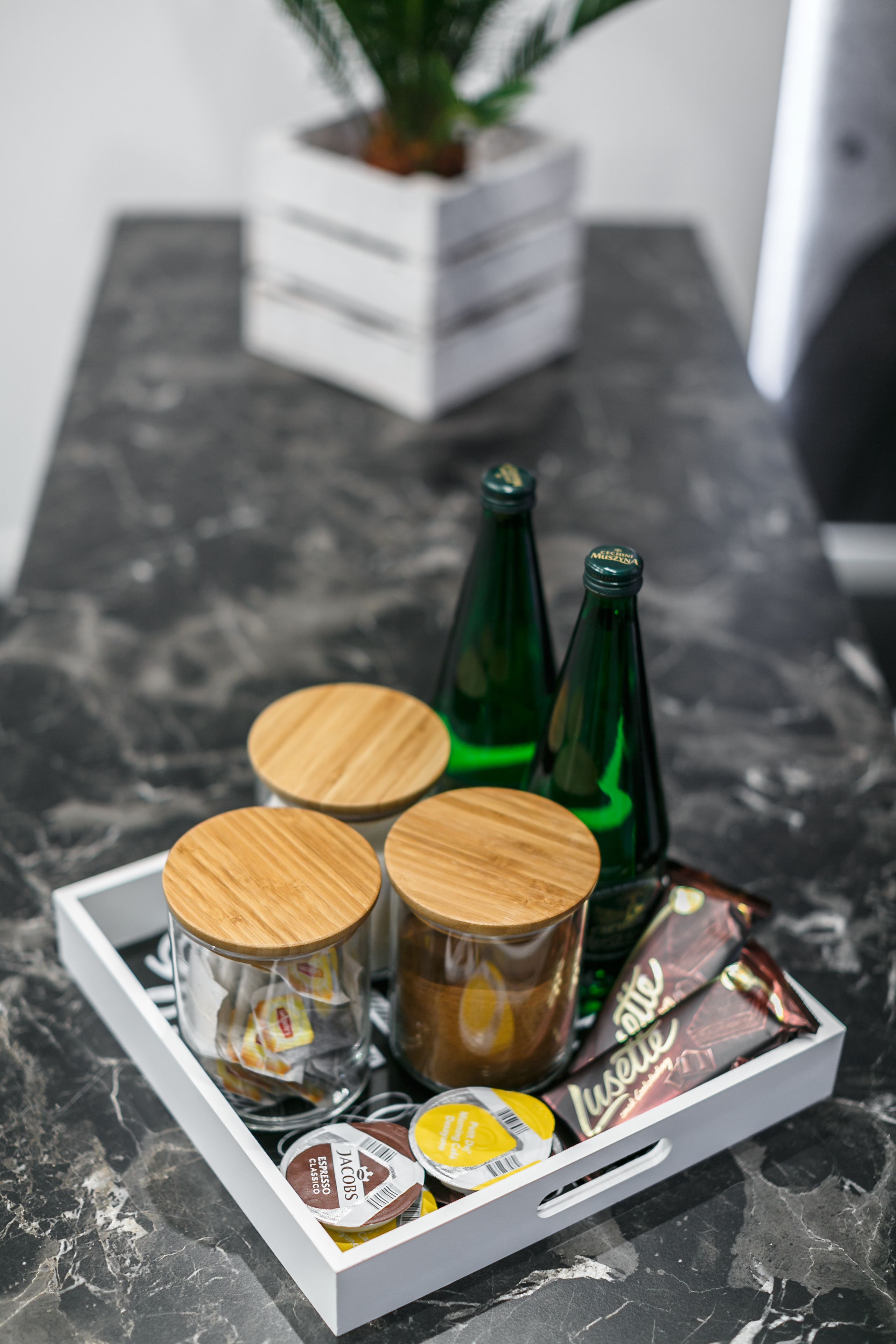 A tray with jars of coffee, chocolate, and green bottles on a marble countertop.