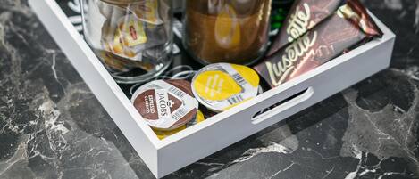 A tray with jars of coffee, chocolate, and green bottles on a marble countertop.
