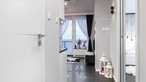 Moderni hotellikäytävä, jossa on valkoiset seinät, kiiltävä musta lattia ja näkymä makuuhuoneeseen, jossa on sänky ja ikkuna.