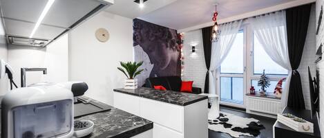 Una cocina moderna con una isla central, un microondas y un horno empotrado. Hay un ventanal con cortinas, una planta en maceta y una alfombra de cuero de vaca.