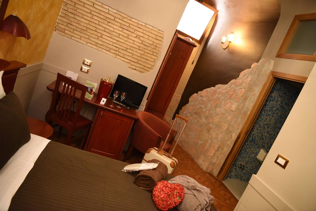 Ein Hotelzimmer mit einem Bett, einem Schreibtisch mit Computer, einem Stuhl, einem Koffer und einem Fernseher.