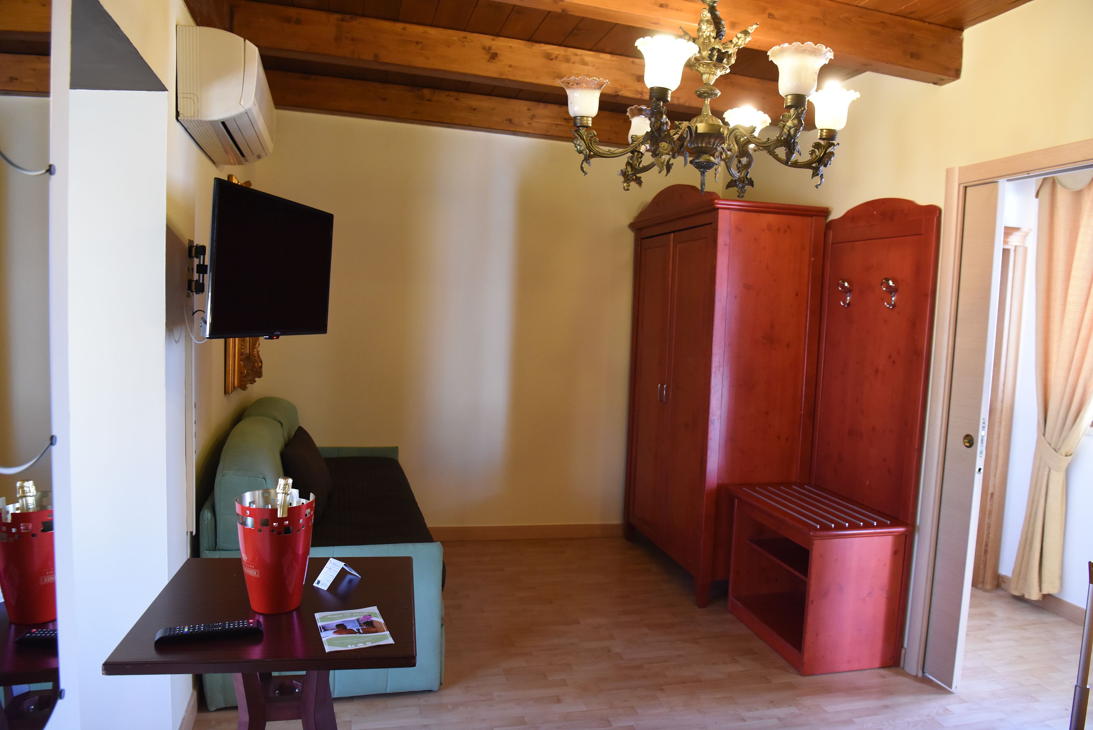 Une pièce avec un plafond en bois, un téléviseur fixé au mur, un meuble rouge, une petite table avec une télécommande et un canapé vert.